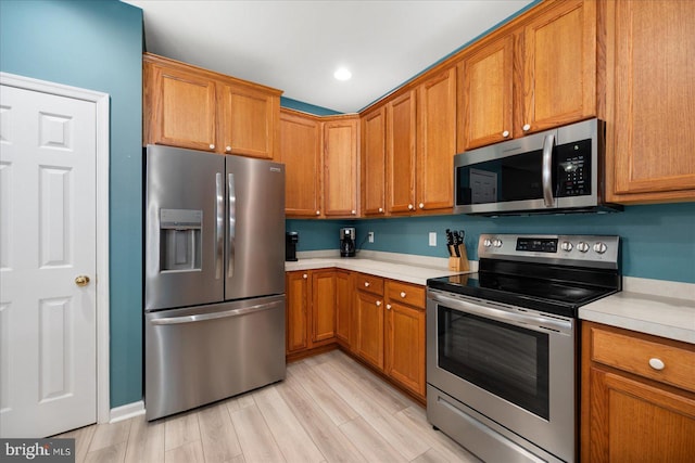 kitchen featuring light wood finished floors, brown cabinets, stainless steel appliances, and light countertops