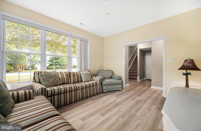 living room with light wood-type flooring, baseboards, a healthy amount of sunlight, and stairs