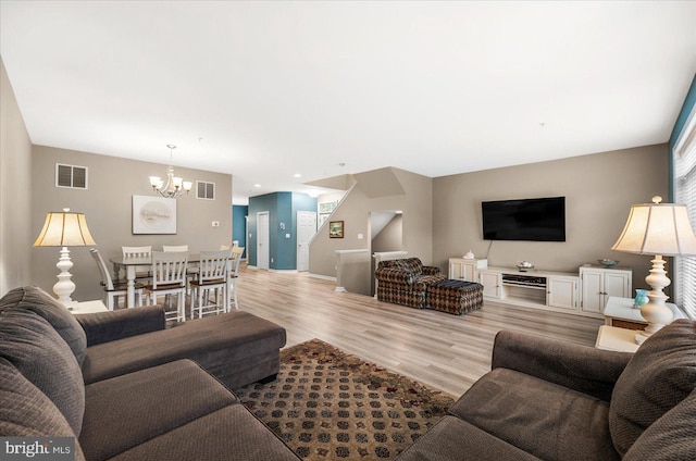 living area featuring visible vents, light wood-style floors, a chandelier, and stairs