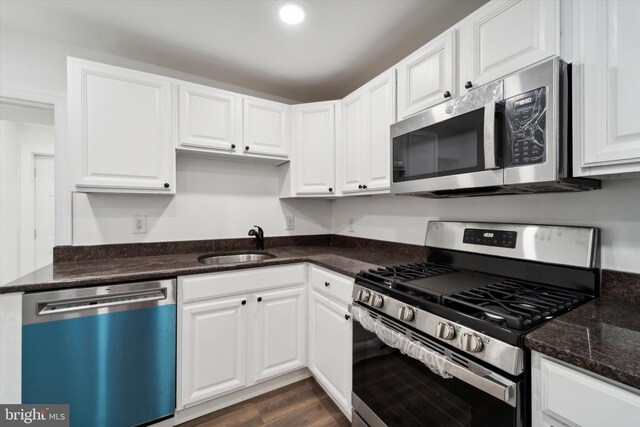 kitchen featuring dark stone counters, sink, white cabinets, appliances with stainless steel finishes, and dark hardwood / wood-style flooring