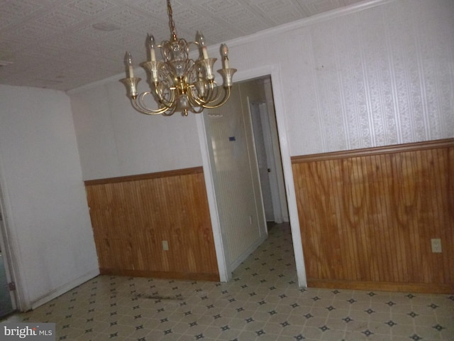 unfurnished dining area with wood walls, a notable chandelier, and ornamental molding