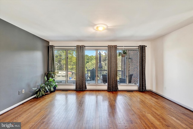 unfurnished room with hardwood / wood-style floors, a healthy amount of sunlight, and baseboards