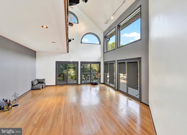 unfurnished living room featuring wood finished floors, baseboards, recessed lighting, track lighting, and a towering ceiling