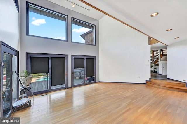 unfurnished living room with stairway, visible vents, wood finished floors, and a towering ceiling