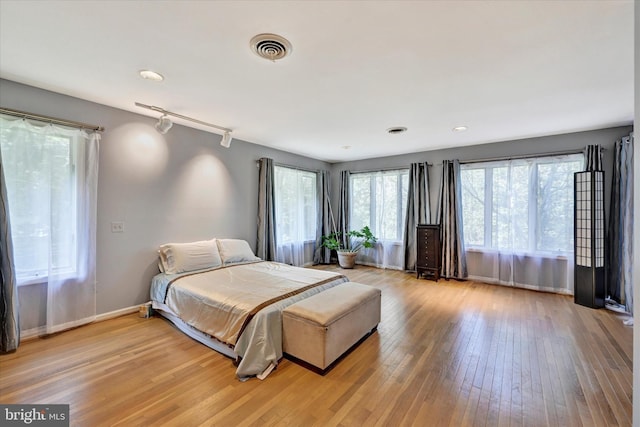 bedroom featuring visible vents, baseboards, rail lighting, and light wood finished floors