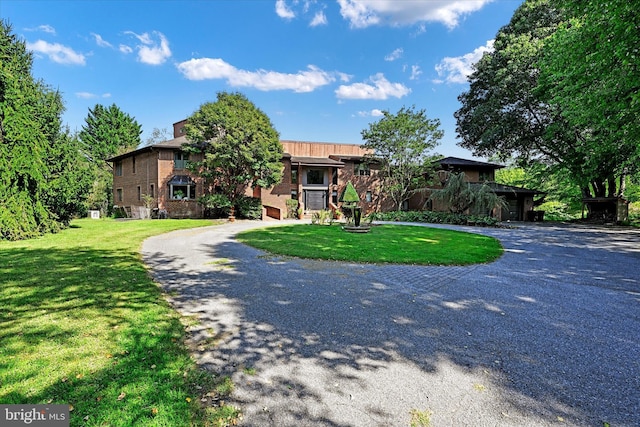 view of front of home featuring brick siding, gravel driveway, and a front yard