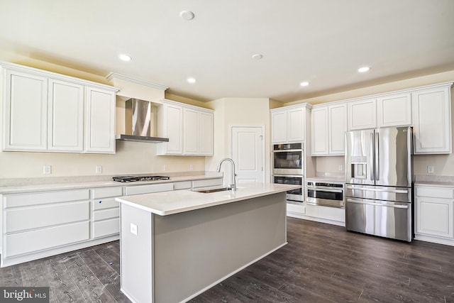 kitchen with white cabinetry, dark wood-type flooring, wall chimney exhaust hood, stainless steel appliances, and a kitchen island with sink