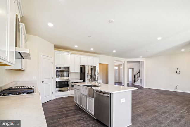 kitchen with sink, white cabinetry, a center island with sink, appliances with stainless steel finishes, and dark hardwood / wood-style flooring