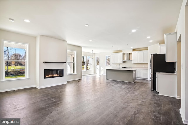 kitchen featuring stainless steel fridge, white cabinetry, dark wood-type flooring, wall chimney exhaust hood, and a kitchen island with sink