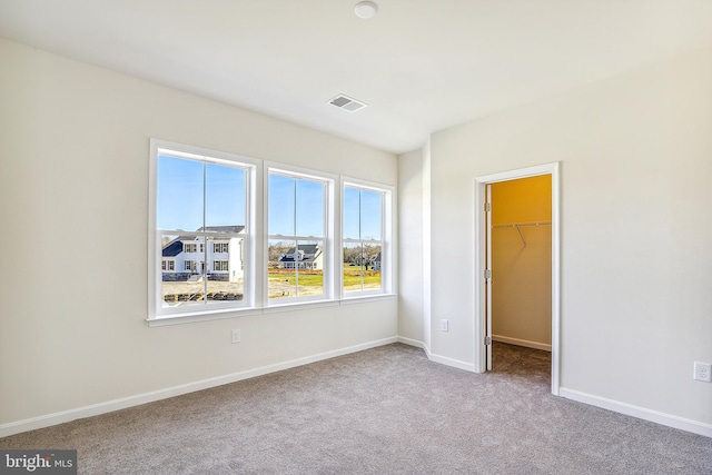 unfurnished bedroom featuring light colored carpet, a walk in closet, and a closet