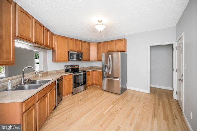 kitchen featuring sink, appliances with stainless steel finishes, light hardwood / wood-style floors, and a textured ceiling