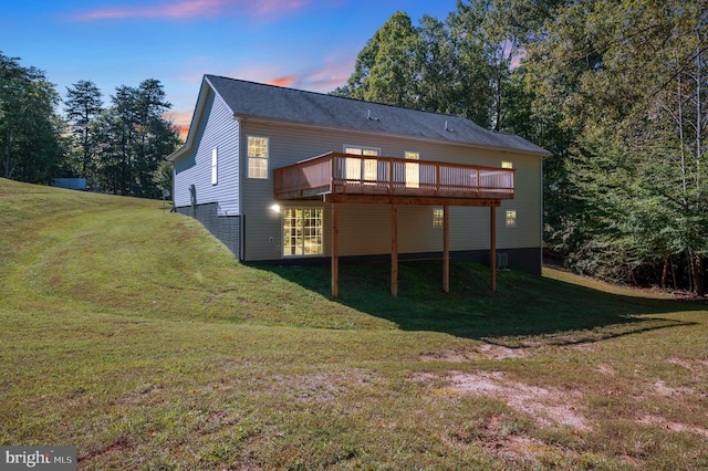 back house at dusk featuring a wooden deck and a lawn