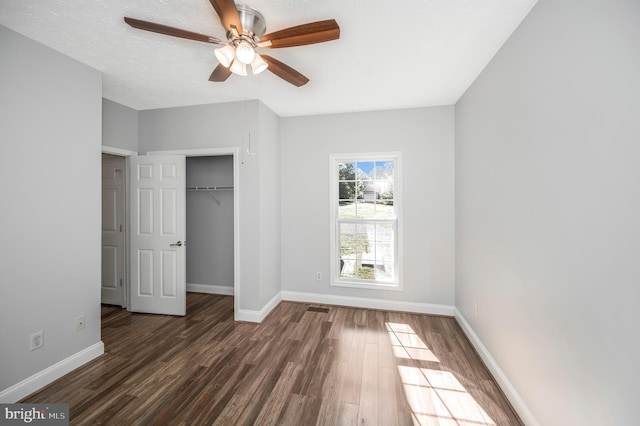 unfurnished bedroom with a textured ceiling, ceiling fan, a closet, and dark hardwood / wood-style flooring