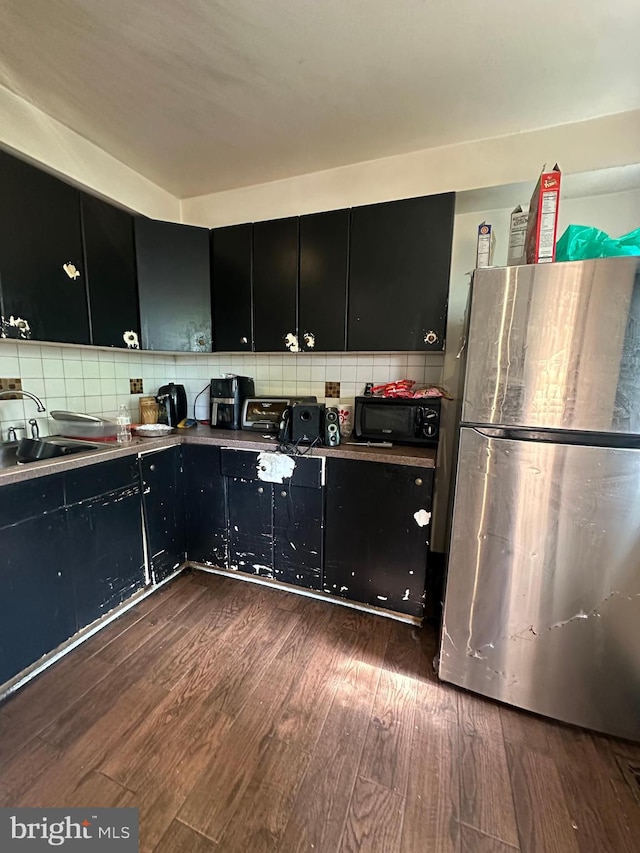 kitchen with dark wood-type flooring, stainless steel fridge, decorative backsplash, and sink