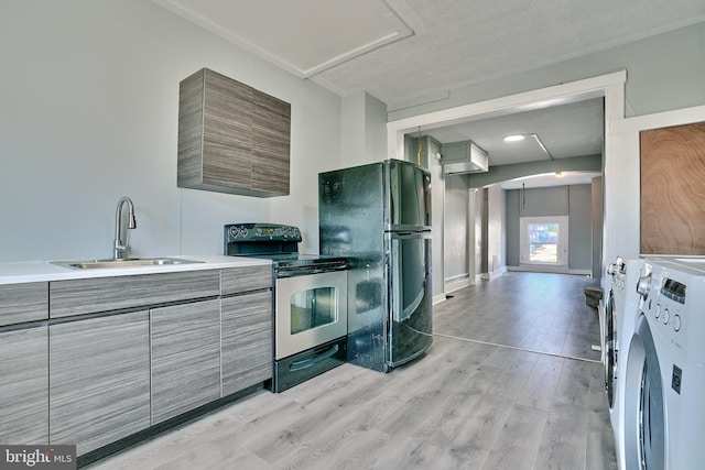 kitchen featuring stainless steel electric range oven, washer / dryer, sink, black fridge, and light wood-type flooring