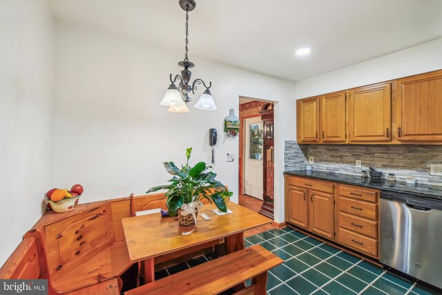 kitchen with decorative backsplash, dark stone countertops, pendant lighting, an inviting chandelier, and stainless steel dishwasher