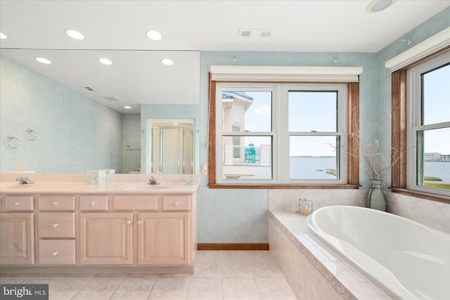 bathroom with a wealth of natural light, vanity, a relaxing tiled tub, and tile patterned flooring