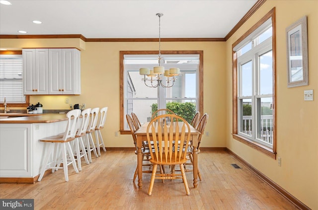 dining space with light hardwood / wood-style floors, a notable chandelier, sink, and crown molding