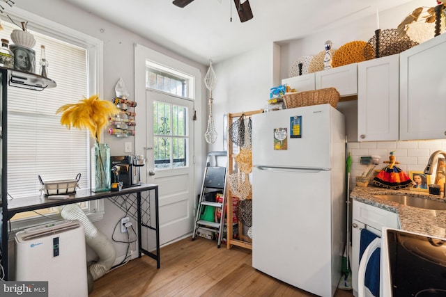 kitchen featuring backsplash, stone counters, light wood-style flooring, freestanding refrigerator, and a sink