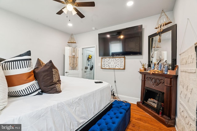 bedroom with a fireplace with raised hearth, ceiling fan, baseboards, recessed lighting, and wood finished floors