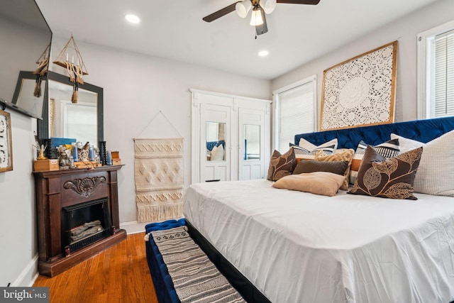 bedroom with a fireplace with raised hearth, ceiling fan, baseboards, recessed lighting, and wood finished floors