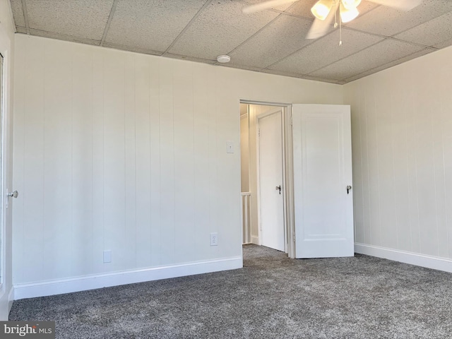 spare room with ceiling fan, a drop ceiling, and dark carpet