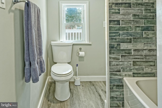 bathroom with hardwood / wood-style flooring, a tub to relax in, and toilet