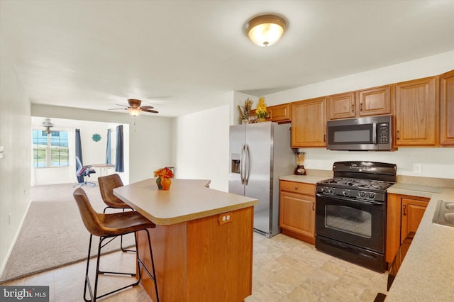 kitchen featuring a kitchen breakfast bar, light carpet, appliances with stainless steel finishes, a center island, and ceiling fan