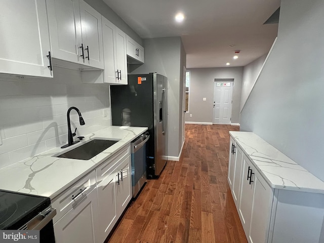 kitchen with appliances with stainless steel finishes, white cabinetry, sink, light stone counters, and dark wood-type flooring