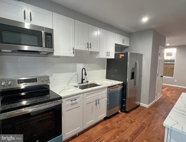 kitchen featuring wood finished floors, a sink, appliances with stainless steel finishes, white cabinetry, and backsplash