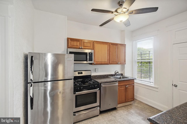 kitchen with baseboards, brown cabinets, appliances with stainless steel finishes, a ceiling fan, and a sink