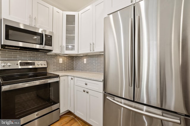 kitchen featuring white cabinets, light wood-type flooring, appliances with stainless steel finishes, light stone counters, and decorative backsplash