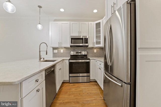 kitchen with pendant lighting, light hardwood / wood-style flooring, sink, appliances with stainless steel finishes, and white cabinets