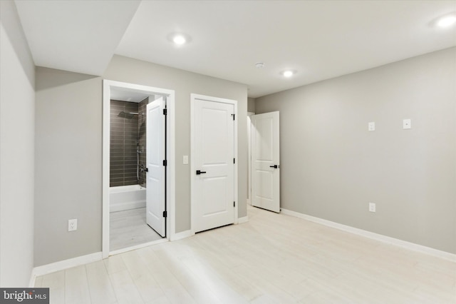 unfurnished bedroom featuring ensuite bath and light hardwood / wood-style floors