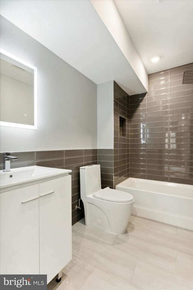 full bathroom featuring tiled shower / bath, vanity, toilet, and tile walls