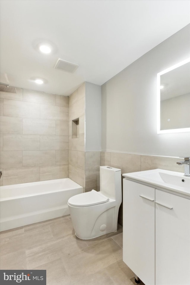 full bathroom featuring tiled shower / bath, vanity, toilet, and tile walls