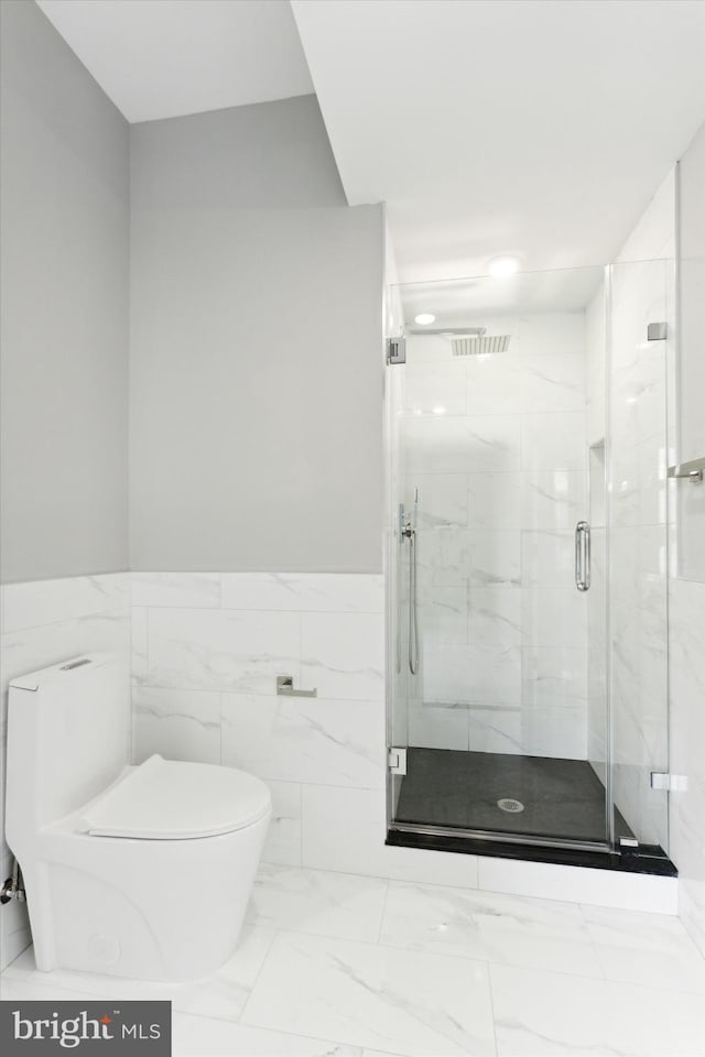 bathroom with tile walls, toilet, and a shower with shower door