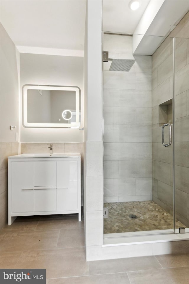 bathroom featuring vanity, a shower with shower door, and tile walls