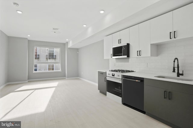 kitchen with gas range oven, white cabinetry, dishwasher, sink, and decorative backsplash