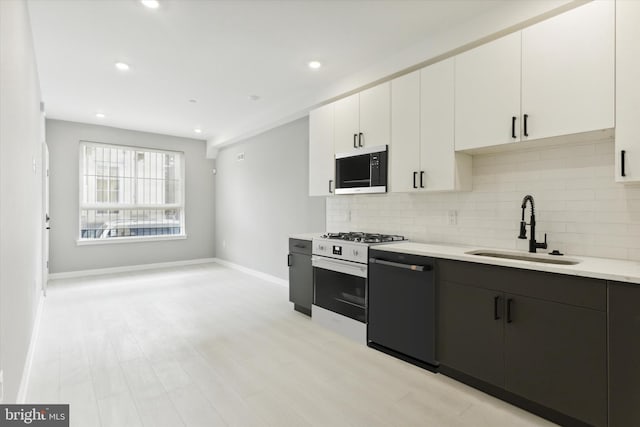 kitchen with black appliances, backsplash, sink, white cabinetry, and light wood-type flooring