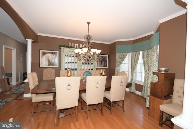 dining area featuring decorative columns, crown molding, wood-type flooring, and a notable chandelier