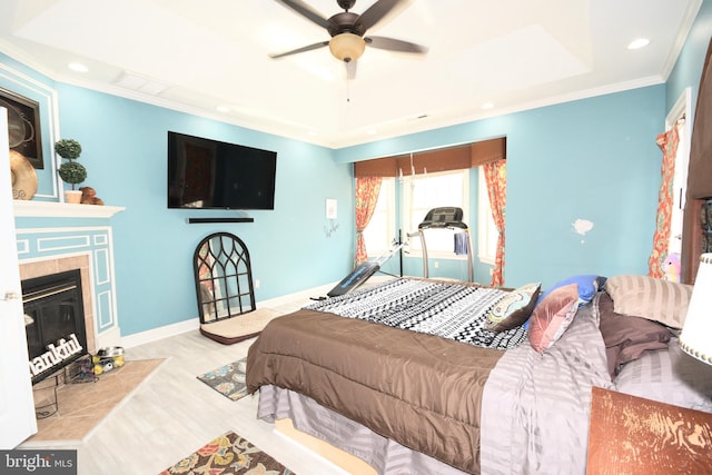 bedroom featuring light hardwood / wood-style floors, ceiling fan, ornamental molding, and a tiled fireplace