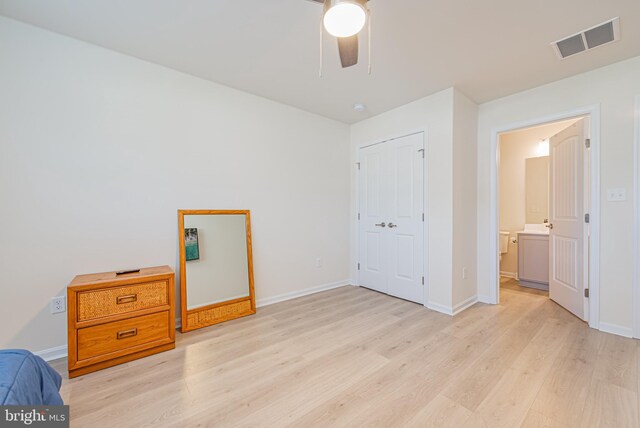 unfurnished bedroom featuring light wood-type flooring, ensuite bath, ceiling fan, and a closet