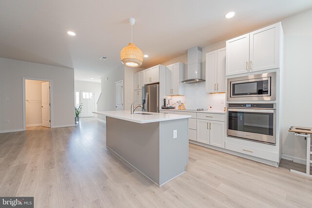 kitchen with pendant lighting, white cabinets, light hardwood / wood-style flooring, wall chimney range hood, and stainless steel appliances