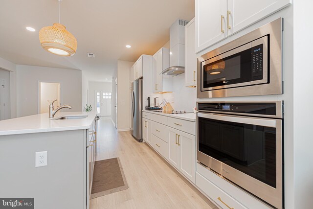 kitchen featuring hanging light fixtures, light hardwood / wood-style flooring, wall chimney range hood, white cabinetry, and stainless steel appliances