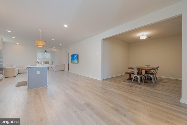 interior space featuring light hardwood / wood-style floors, a breakfast bar, pendant lighting, a kitchen island with sink, and sink