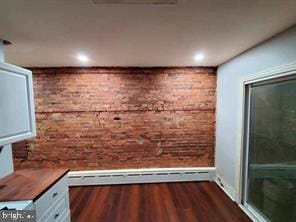 interior space with brick wall, a baseboard radiator, and hardwood / wood-style flooring