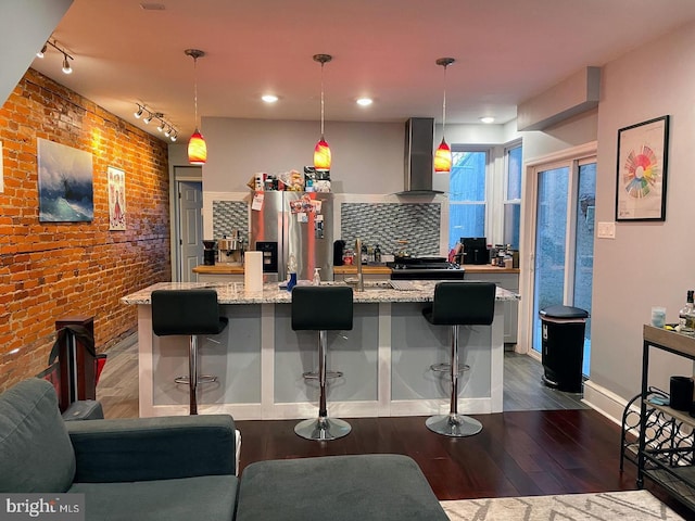 kitchen with dark hardwood / wood-style flooring, a breakfast bar, hanging light fixtures, and wall chimney range hood