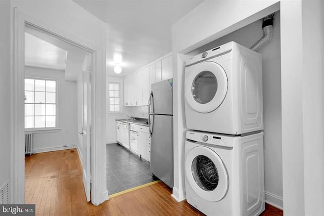 laundry room featuring radiator, hardwood / wood-style flooring, and stacked washer and dryer