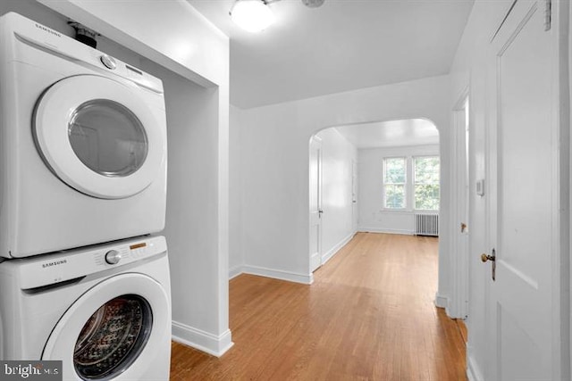 laundry room featuring stacked washer and clothes dryer, radiator heating unit, and light hardwood / wood-style flooring